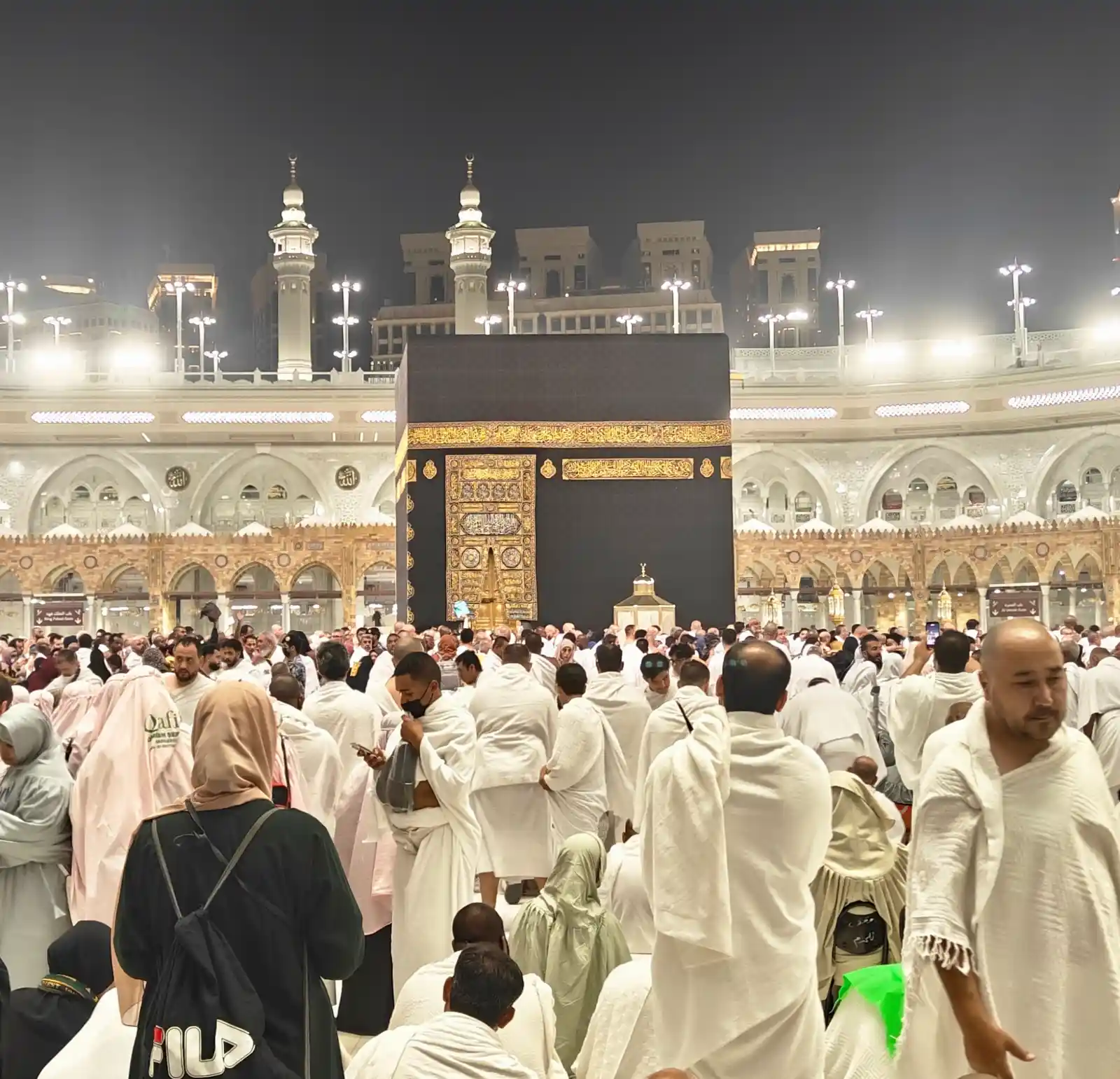The Kaaba at Masjid al-Haram in Makkah illuminated at night, surrounded by Muslim pilgrims performing Umrah in ihram.